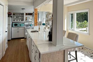 A kitchen with white cabinets, a marble countertop, a sink, and a window with a view of greenery.