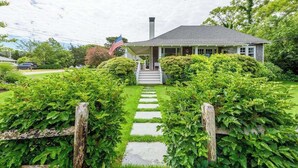 Uma casa com varanda, uma bandeira e um jardim bem cuidado.