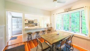 Cozinha com área de refeições, geladeira, micro-ondas e janela com vista para o verde.