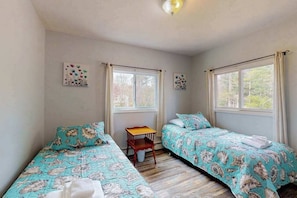 A room with two beds, a small table, and two windows.