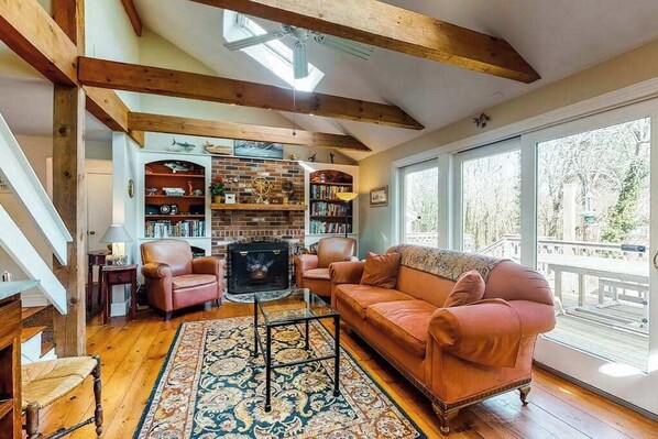 A cozy living room with a fireplace, leather furniture, and a large window overlooking a deck.