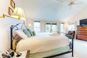 A bedroom with a bed, bedside lamps, a dresser, a television, and a ceiling fan.
