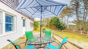 Un patio con una mesa redonda y sillas, un paraguas a rayas y una valla de madera.