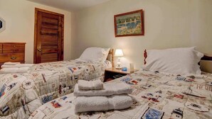 Una habitación de hotel con dos camas, una puerta de madera, un cuadro en la pared y una mesita de noche con una lámpara.