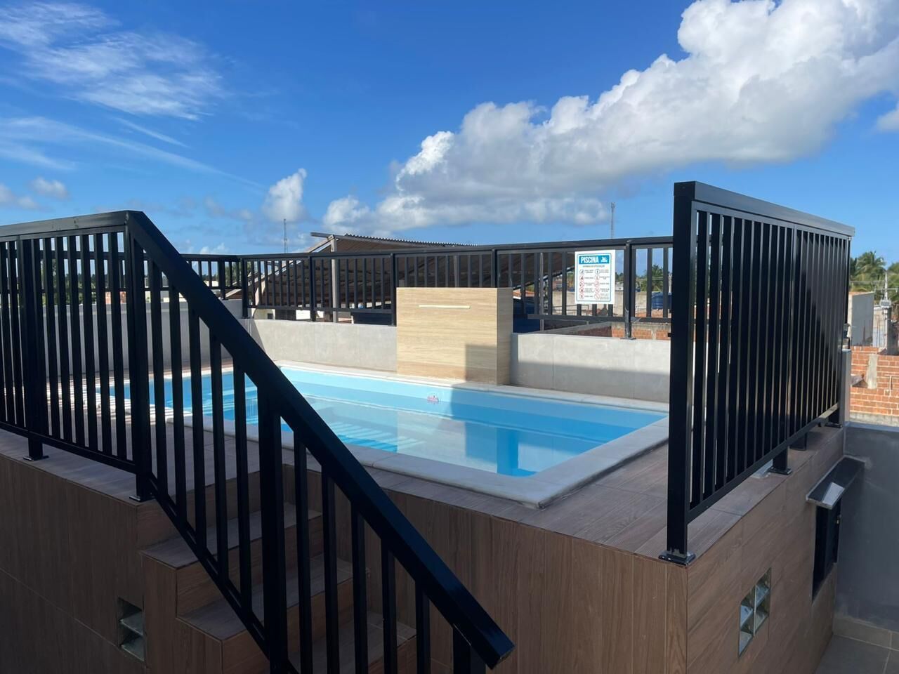 En pool på taget med træterrasse og sorte gelændere.