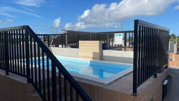 En pool på taget med træterrasse og sorte gelændere.