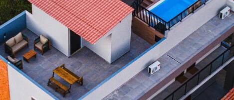 A modern building with a rooftop pool, outdoor seating, and a covered area with umbrellas.