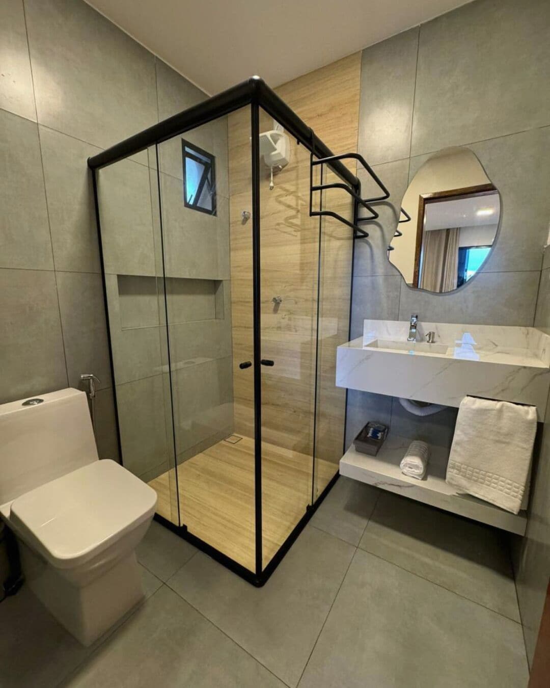 A modern bathroom with a glass-enclosed shower, a white toilet, a sink with a mirror, and a towel rack.