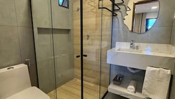 A modern bathroom with a glass-enclosed shower, a white toilet, a sink with a mirror, and a towel rack.