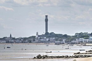 Un pueblo costero con un faro destacado, una playa de arena y barcos.