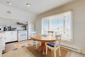 Une cuisine avec des meubles blancs, une cuisinière et une table à manger avec des chaises.