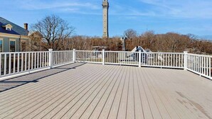 Eine Holzterrasse mit weißen Geländern, ein Stein-Turm im Hintergrund und kahl stehende Bäume.