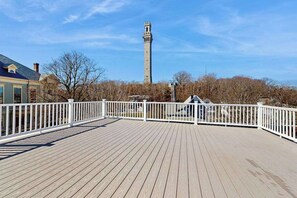 Une terrasse en bois avec des balustrades blanches, une tour de pierre en arrière-plan et des arbres sans feuilles.