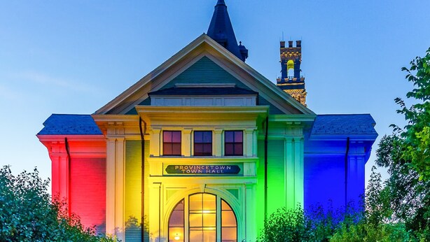 Ein Gebäude mit einem Schild, auf dem 'Provincetown Town Hall' steht, und einem Kirchturm im Hintergrund.