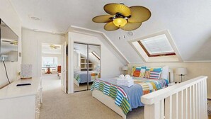 Ein Schlafzimmer mit einem Bett, Deckenventilator, Dachfenster und einer weißen Geländer.