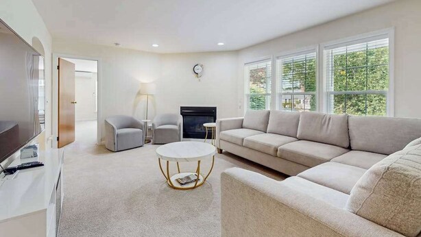 A modern living room with a sofa, a round coffee table, a fireplace, and large windows. - Comfortable family getaway near the beach with patio, grill, WiFi and AC (West Yarmouth)