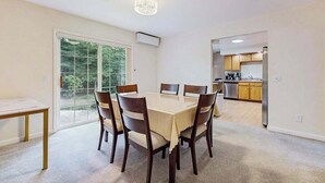 A dining area with a table and chairs, a chandelier, and a view through a glass door to a kitchen. - Comfortable family getaway near the beach with patio, grill, WiFi and AC (West Yarmouth)