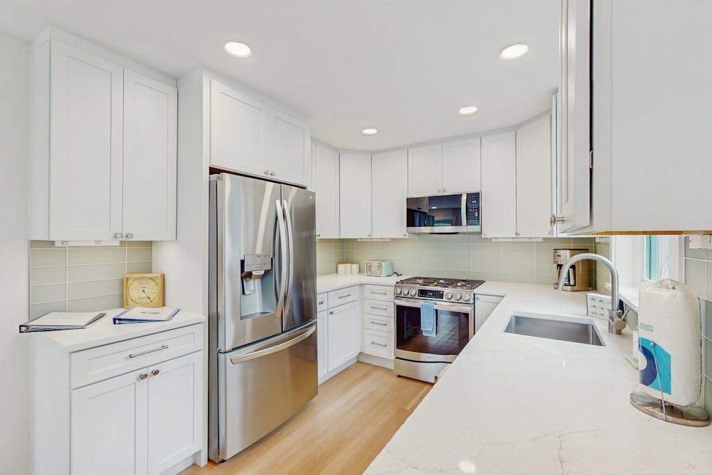 A modern kitchen with white cabinetry, stainless steel appliances, a microwave, and a sink.