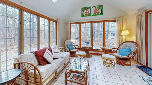 A sunlit room with large windows, wicker furniture, and a ceiling fan. - Quiet home with sunroom, deck, W/D, AC, & quick access to beach (Wellfleet)