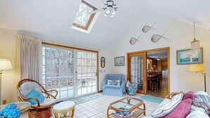 A spacious living room with wicker furniture, a dining area, and a view through large glass doors. - Quiet home with sunroom, deck, W/D, AC, & quick access to beach (Wellfleet)