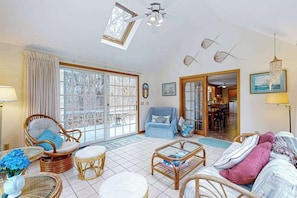 A spacious living room with wicker furniture, a dining area, and a view through large glass doors. - Quiet home with sunroom, deck, W/D, AC, & quick access to beach (Wellfleet)