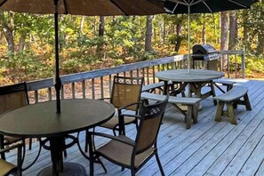 An outdoor deck with a round table and chairs, a grill, and a view of a wooded area. - Quiet home with sunroom, deck, W/D, AC, & quick access to beach (Wellfleet)