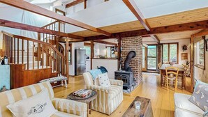 A spacious living area with a wooden staircase, a fireplace, and a dining table. - Nana’s Treehouse | House with spacious deck, grills, outdoor shower & W/D (West Tisbury)