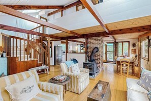 A spacious living area with a wooden staircase, a fireplace, and a dining table. - Nana’s Treehouse | House with spacious deck, grills, outdoor shower & W/D (West Tisbury)
