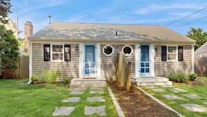 Una casa de una planta con porche delantero, un jardín pequeño y cielo despejado.