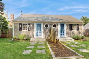 A single-story house with a front porch, a small garden, and a clear sky.
