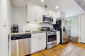 A modern kitchen with white cabinets, stainless steel appliances, and a wooden floor.