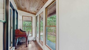 Una habitación con techo de madera, ventanas amplias, un piano y una silla.