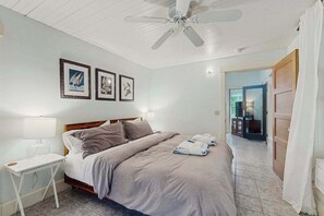 A bedroom with a bed, a bedside table, a ceiling fan, and framed pictures on the wall.