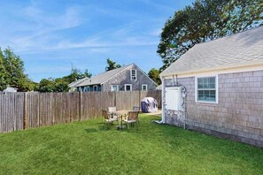 Ein Garten mit Holzzaun, Rasen und einer kleinen Terrasse mit Stühlen.