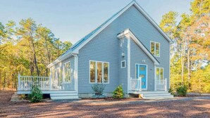 Ein zweistöckiges Haus mit Veranda, einer blauen Tür und einem kleinen Garten.