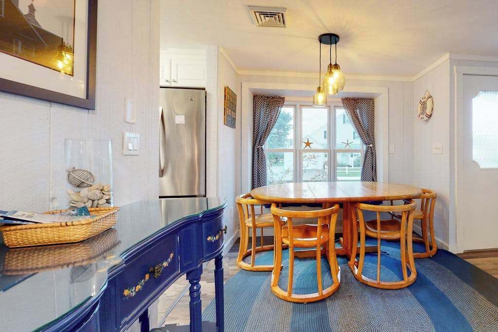 A dining area with a round wooden table and chairs, a refrigerator, and a window with curtains.