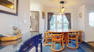 A dining area with a round wooden table and chairs, a refrigerator, and a window with curtains.