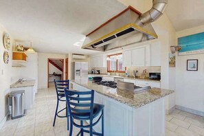 Cocina moderna con una isla central, muebles color blanco y una campana extractora de acero inoxidable.