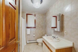 Een badkamer met een houten deur, een witte wastafel, een toilet en een douche.