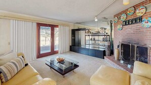 Sala de estar com sofá, mesa de centro e lareira. Cozinha visível ao fundo, com geladeira e armários.