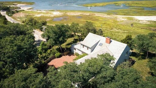 Uma casa com telhado inclinado, rodeada por vegetação densa e vista para o oceano.