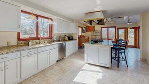 Uma cozinha espaçosa com armários brancos, uma ilha central e um espaço de refeições com cadeiras.
