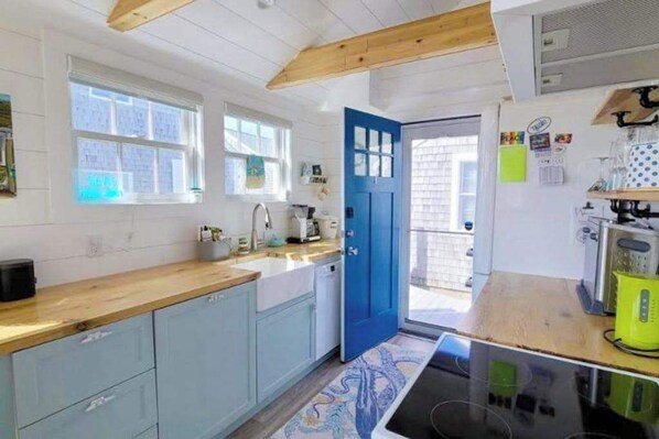 Eine Küche mit hellblauen Schränken, einer Holz Arbeitsplatte, einer blauen Tür und Blick ins Freie.