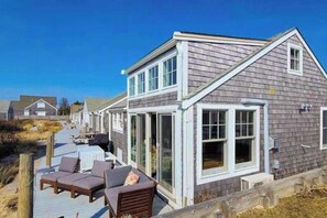 Ein Küstenhaus mit Terrasse, großem Fenster und kleiner Veranda.