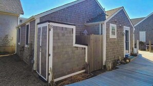 A residential building with a garage, a wooden deck, and a fenced yard. - Peaceful Beachfront Cottage with Bay Views: near town, bike trails & dune walks (North Truro)