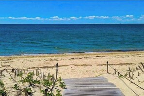 Ein hölzerner Steg führt zu einem Sandstrand mit freiem Blick auf den Ozean.
