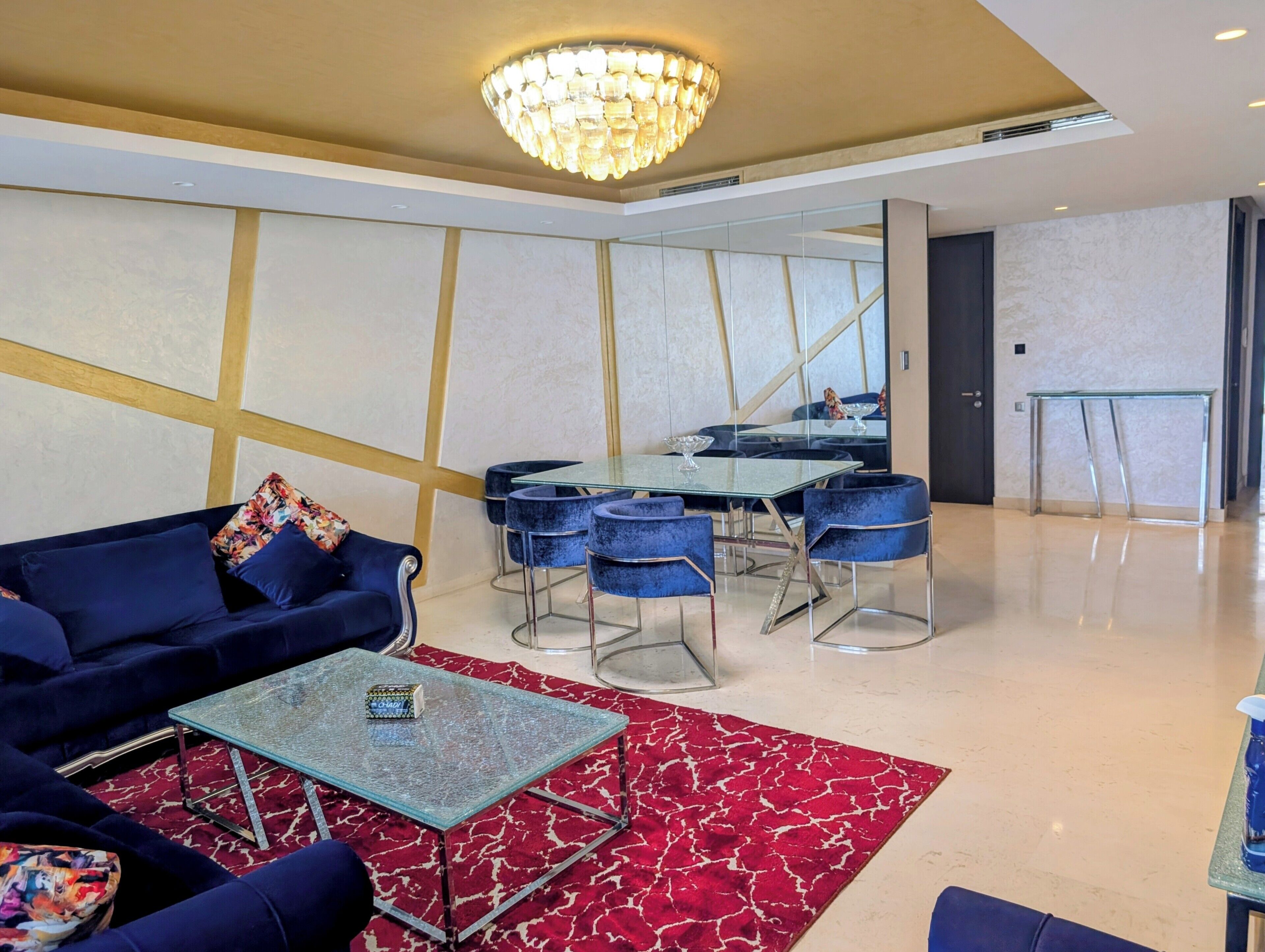 A modern hotel lobby with a blue sofa, a glass table, and a red patterned rug.