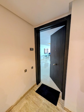 Ein Korridor mit einer Tür, auf der '302' steht, die zu einem Zimmer mit einem Bett und einem Sessel führt.