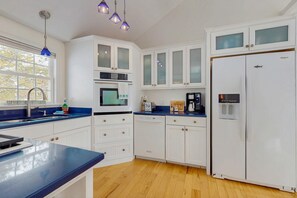 Eine Küche mit weißen Schränken, einer blauen Arbeitsplatte, einem Geschirrspüler, einem Kühlschrank und einem Fenster mit Blick auf Bäume.