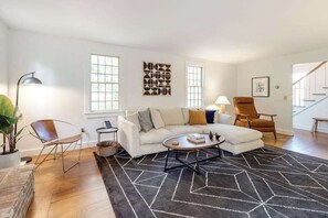 A living room with a sofa, two chairs, a coffee table, a rug, and a staircase. - Peaceful half-acre home near ocean, dining & shops and a fire pit (Wellfleet)